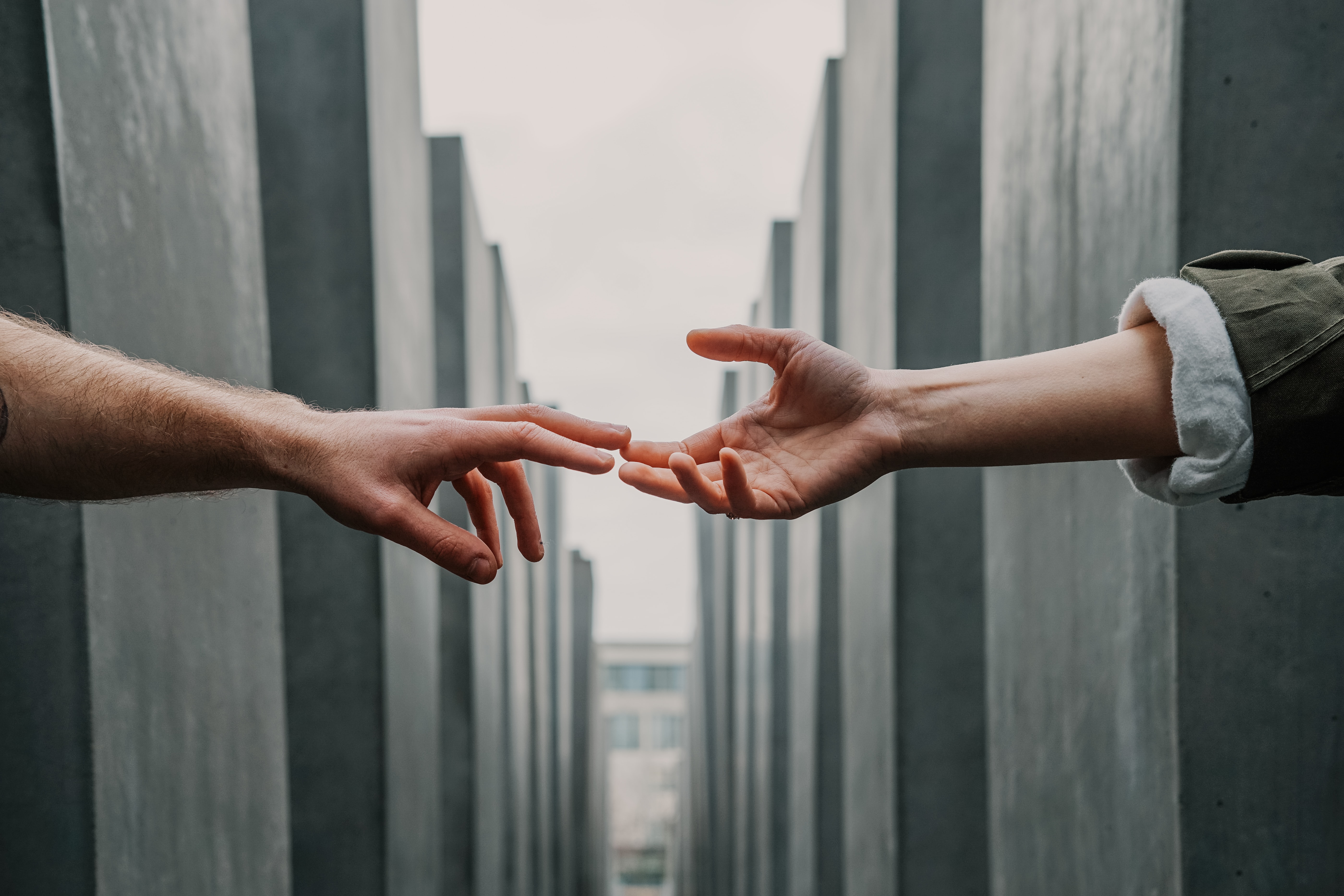 hands reaching for each other, fingers just touching, with grey block stones in the background